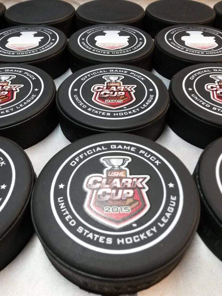 Stack of hockey pucks branded “USHL Clark Cup 2015” and “Official Game Puck”