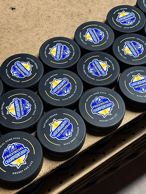 Stack of hockey pucks branded “Provincial Championships” on a cardboard surface